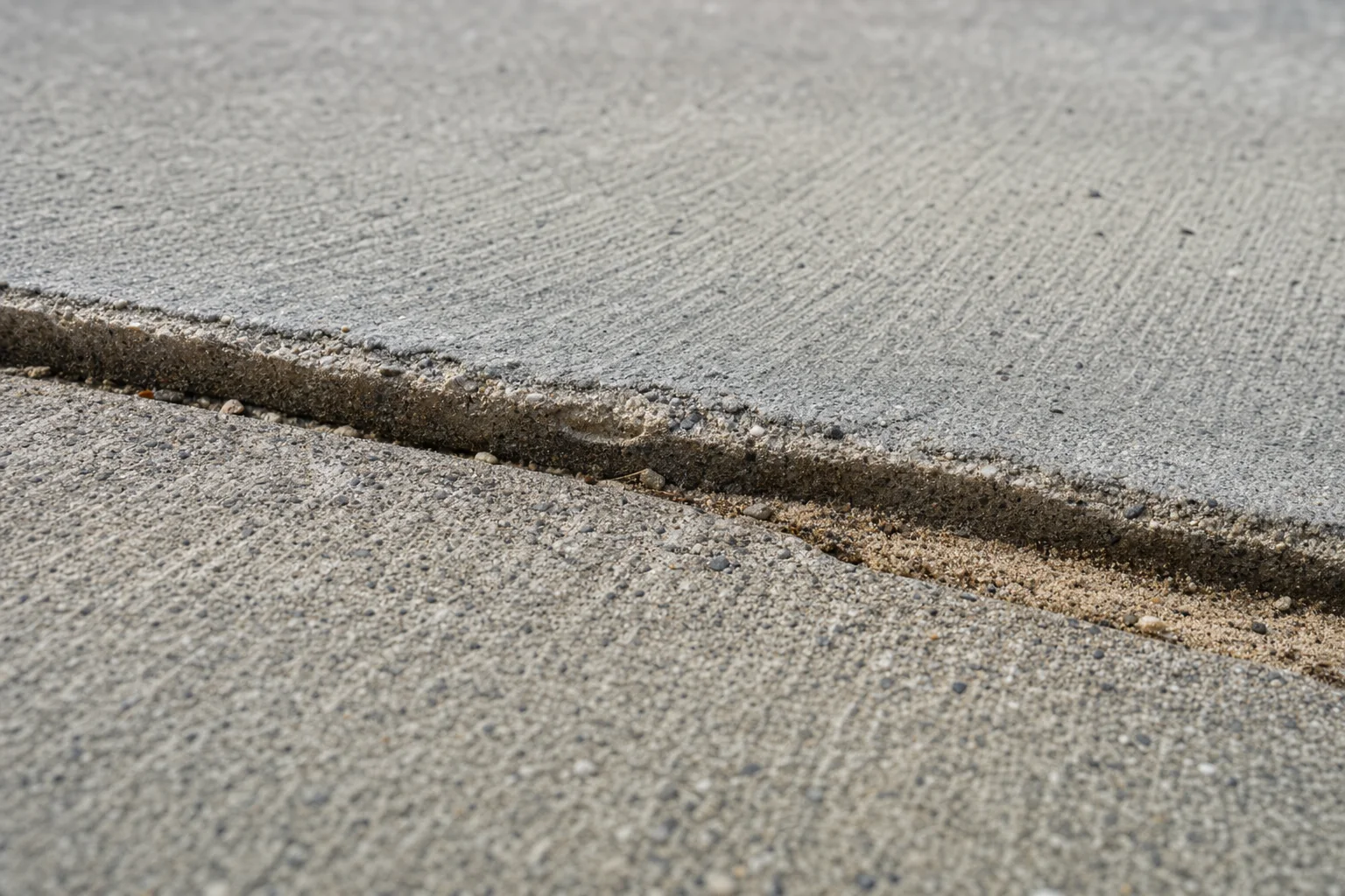 Close view of a joint across a concrete driveway where one side sits lower than the other, forming a small step.